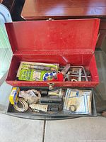 Toolbox open showing contents: wrenches, packaged drain tool, sealant tube, hardware, wire