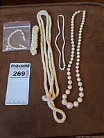 All four jewelry pieces laid out: three necklaces, one bracelet in bag