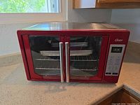 Front view of red Oster digital convection toaster oven showing doors, control panel, and accessories inside