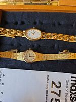 Front view of both gold tone women’s watches in display tray