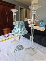 Two tall clear glass candlesticks and one teal mosaic candle lamp on table