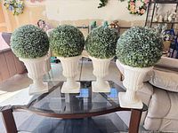 Four resin/concrete urns each with a spherical artificial topiary ball displayed on a glass table