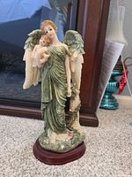Front view showing angel holding child, gown, wings, column, wood base
