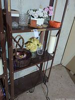 Shelving view of most items including glass, ceramic, basket, artificial flowers, candle, metal stand on bottom shelf