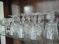 Shelf containing grouped upside-down cordial size cut-crystal glasses and a few coupe style pieces