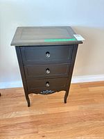 Front view showing three drawers, black finish, metal knobs, decorative apron