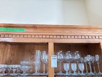 Cabinet shelf with multiple styles of clear stemware including pressed goblets, rounded wine glasses, smaller wine glasses
