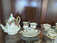Floral bone china teapot, creamer, sugar bowl, teacups, saucers, serving plate displayed in cabinet