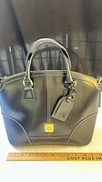 Front view of black leather Dooney & Bourke satchel with ruler for scale