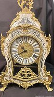 Front view of ornate gilded brass mantel clock displaying dial and inlay details