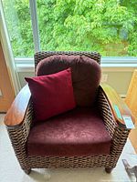Front view of wicker armchair with burgundy cushions and accent pillow