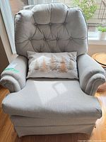 Front view of light gray tufted swivel armchair with pillow