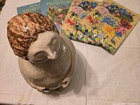 Overhead view of glazed ceramic figurative sculpture with three illustrated books behind it