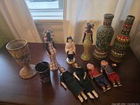 Group shot of entire lot on tabletop: vases, goblet, tumbler, figurine, five dolls