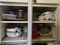 Cupboard view showing ActiFry, red ramekins, clear glass bakeware, milk-glass casseroles, plastic containers, jars and bottles