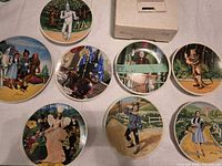 Eight Wizard of Oz plates laid out with one shipping box visible