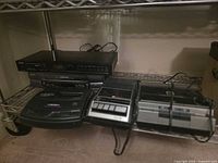 Shelf with Akai tuner, Sanyo VCR, black A/V component, cassette recorder and grey console