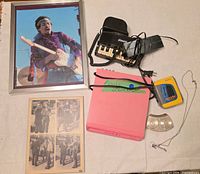 All seven items laid out together: framed Hendrix poster, wall plaque, Sony Walkman, Pianotel phone, Electrohome player, belt buckle, necklace