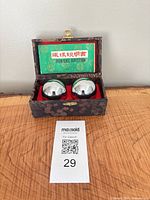 Open box showing two chrome Baoding balls, red interior, green instruction sheet
