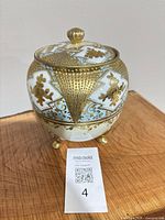 Front view of porcelain biscuit jar on three gilt feet with lid in place showing gold and blue decoration
