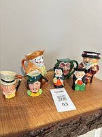 Group shot of all seven ceramic miniature character jugs on wooden surface