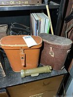 Two leather binocular cases (one brown, one tan) shown beside olive-drab angle flashlight