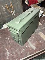Exterior view of olive drab metal ammunition box showing hinged lid, latch and handle
