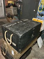 Top and side view of black wooden military box with rope handle and stencilled lettering