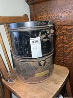 Two stacked black metal military hat boxes showing overall form and wear