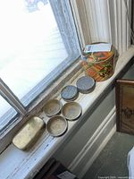 Overall view of all items on windowsill: decorative tin, brass case, three brass coasters, military sunburn tin