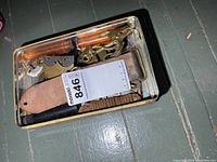 Top view of tin with assorted parts including leather strap, cord, plastic grips, brass hardware