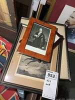 Stack of framed items showing portrait photograph, small dark frame, equestrian print and additional frame underneath