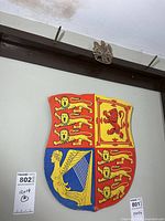 Paperboard UK coat of arms shield hanging on wall with small metal crest badge above