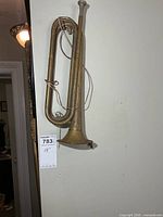Full view of brass Boy Scouts bugle hanging on wall with measurement tag