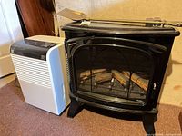 Front view of electric stove fireplace alongside white 50-pint dehumidifier and brass spade on stove top