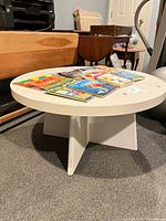 Full view of white/cream round kids coffee table with books on top