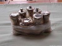 Front view of four silver shakers and three grinders wrapped in plastic