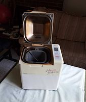 Bread maker lid open showing loaf pan and kneading paddle