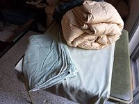 Rolled beige feather comforter atop table with detached folded pale green cover