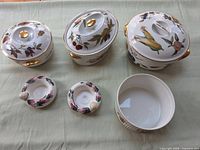 All six porcelain pieces arranged on table showing fruit motifs and gold trim