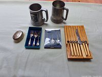Overall lot showing steak knives, carving knife, two metal beer mugs, baby cutlery sets and oval brush laid on table