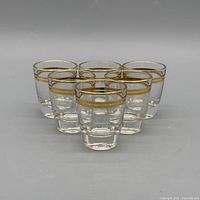 front view of six clear glass shot glasses with gold bands