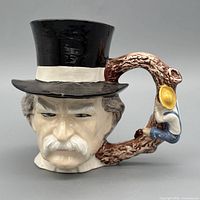 Front view of ceramic Toby jug showing gentleman’s face, top hat, and tree branch handle with small figure