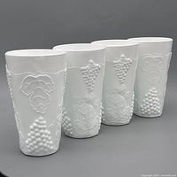 Four white milk glass tumblers with embossed grape pattern front view