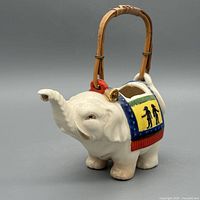 Left side profile of elephant teapot showing trunk spout, saddle decoration, bamboo handle