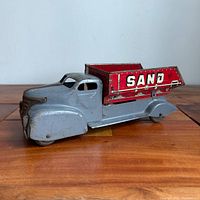 Left front three-quarter view showing cab, dump bed and SAND lettering