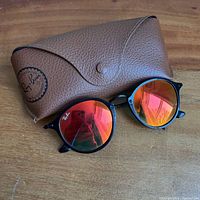 Sunglasses with case showing frame color, lens mirror, and case logo