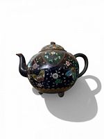 Front angled view showing teapot shape, tripod feet and enamel decoration