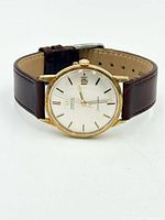 Front view showing dial, gold bezel, date window, leather strap