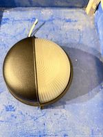 Front view of round sconce showing half black cover and frosted ribbed lens